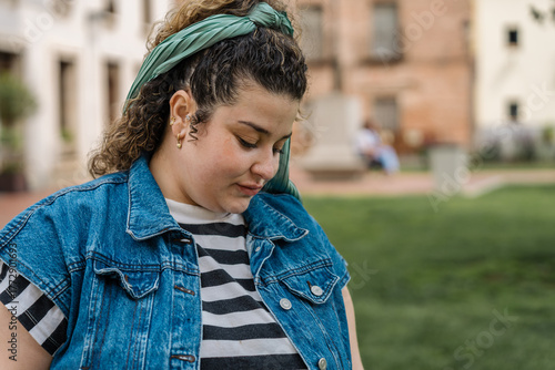 Young woman wearing denim vest looking down contemplating in urban park