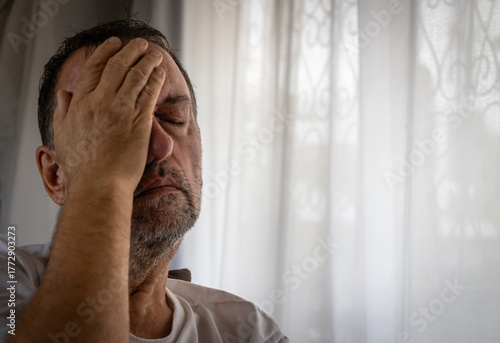 Tired middle-aged man covering his face with hand feeling stressed at home.