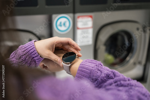 Young woman checking smartwatch while waiting for laundry in laundromat