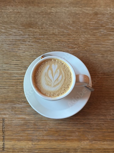 Coffee cup on coffee shop wooden table background. Vertical UGC content photo, cappuccino with foam drink top view, no people cozy scene
