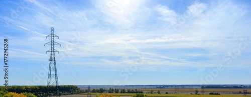 Huge electricity tower overlooking a flat rural landscape to the horizon on a clear sunny day with a blue sky and wispy clouds in the background.