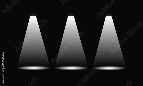 Three bright white spotlight beams illuminate a dark stage or backdrop from above.
