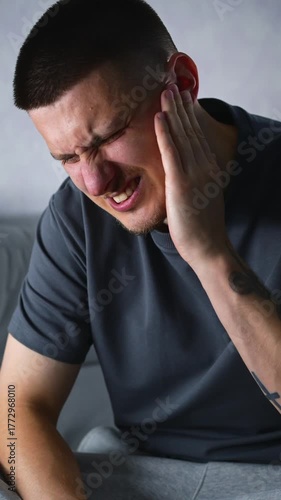A man in a gray T-shirt sitting on a gray sofa in a room has an earache.
The man is holding on to the pain and is in no hurry to see a doctor.
Treatment for hearing problems