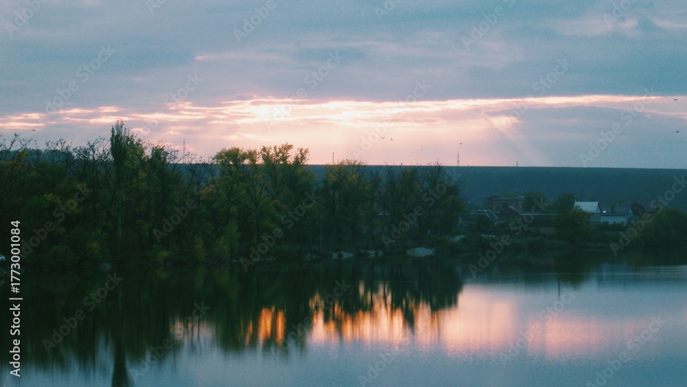Obraz premium Evening light breaking through clouds over calm reflective lake