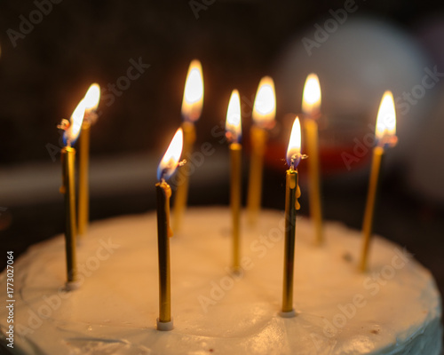 Close-up of a birthday cake with white frosting and several lit golden candles, casting a warm glow, capturing the festive and intimate atmosphere of a celebration