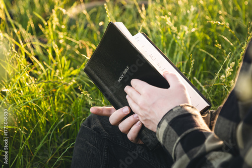 Wall Mural Man is holding the holy Bible in a field during sunset, concept for faith, spirituality, and religion