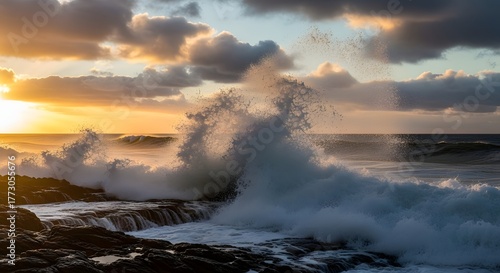 Spectacular sunset over the ocean with large waves crashing against the rocky coast, creating a powerful and scenic seascape