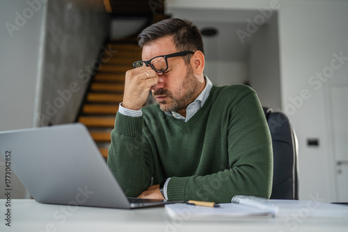Stressed man experiencing headache while working on laptop