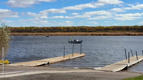A fishing boat with an outboard motor goes past a landing with two docks on the Rainy River, which borders the United States and Canada, near Baudette, Minnesota on a sunny autumn morning.