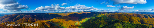 Mountain panorama in autumn colors, with an alternation of deciduous forests with golden foliage and green coniferous forests. Aerial view of the Carpathian mountains with cloud shadows in autumn