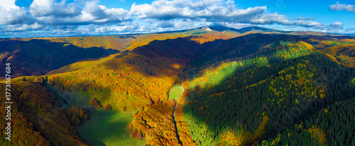 Mountain panorama in autumn colors, with an alternation of deciduous forests with golden foliage and green coniferous forests. Aerial view of the Carpathian mountains with cloud shadows in autumn