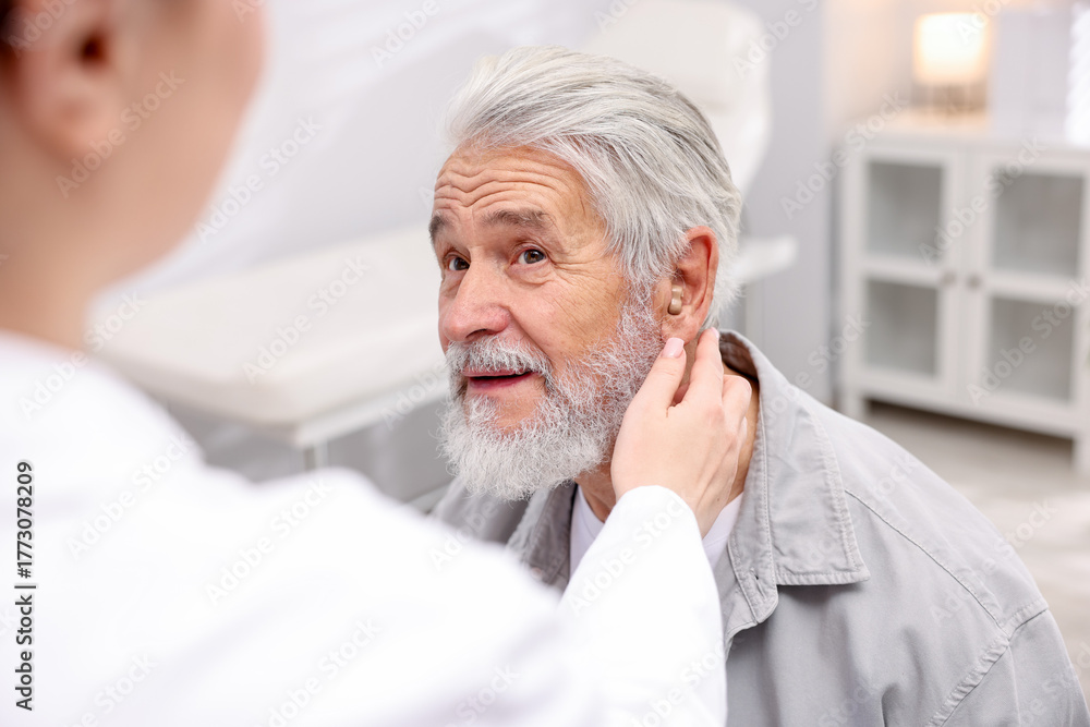 © New Africa - Doctor putting hearing aid into senior man's ear in hospital, closeup