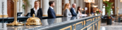 Golden service bell on a marble reception desk in a luxury hotel lobby with staff and guests in the background. Hospitality and accommodation concept.