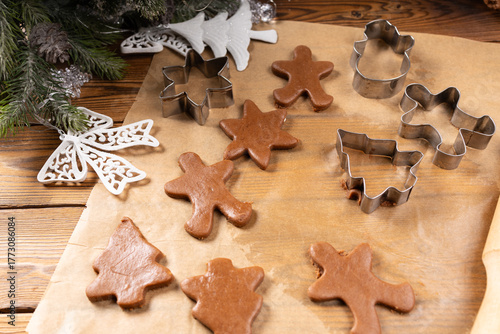 Rolled ginger dough on parchment paper, On the wooden surface there are metal gingerbread molds and a rolling pin.