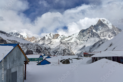 Scenic view of lodges at Annapurna Base Camp covered in snow. The majestic Himalayan mountains form a beautiful backdrop on a cloudy day in Nepal.