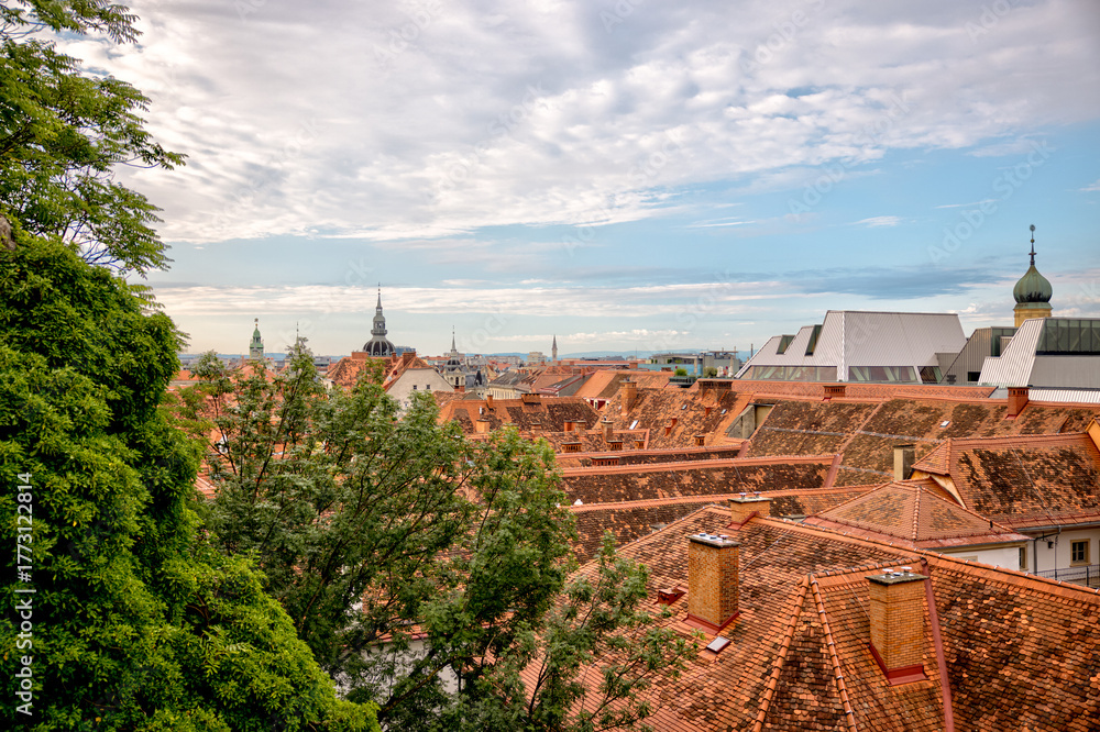 Obraz premium Graz, Austria – July 22, 2025: A view of the city’s rooftops and skyline from the Schlossberg hill, offering a picturesque overlook of the urban landscape below. 