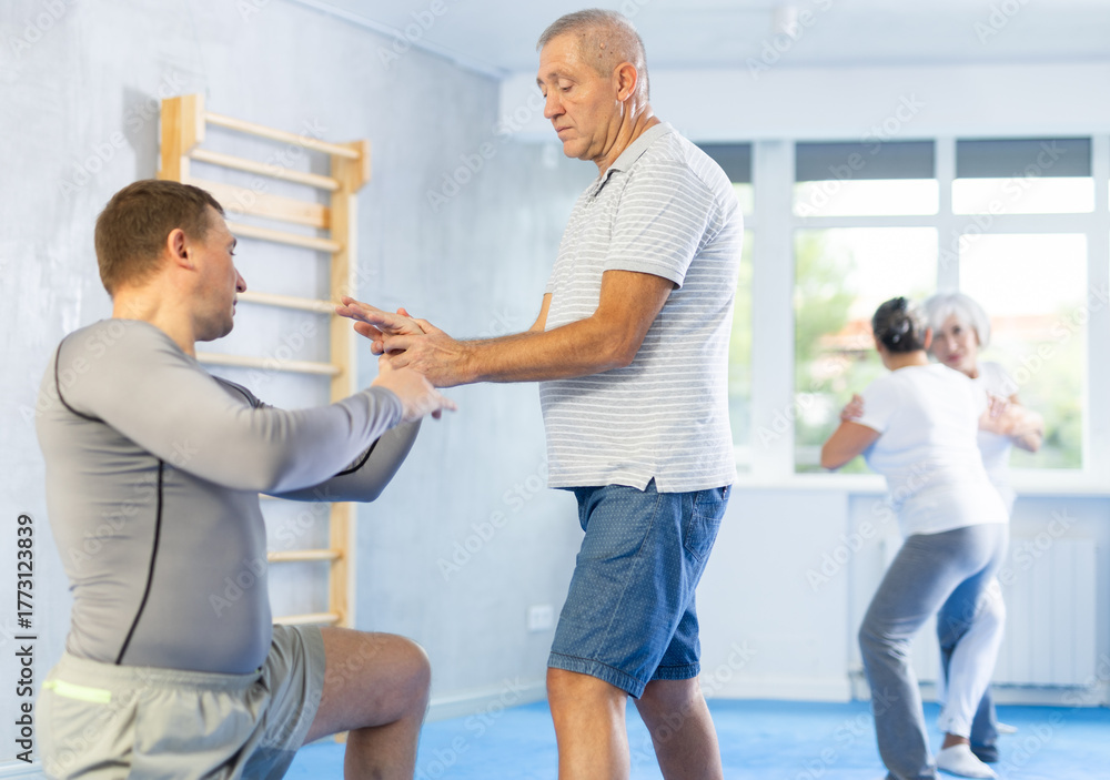 Obraz premium Senior man train in pair with middle-aged coach to strike and reflect blows of enemy. Intense moment as two individuals engage in self-defense training, showcasing skill, reaction, repulse