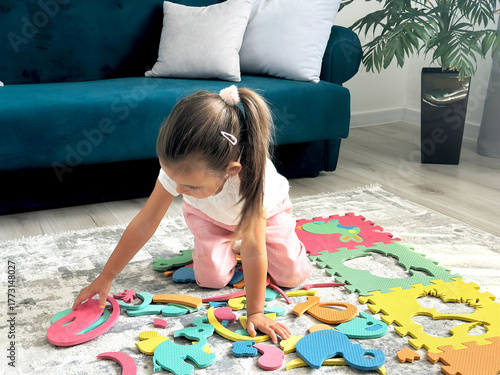 Beautiful cute little girl is putting together an educational puzzle mat.