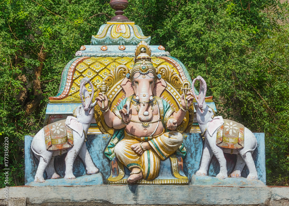 Obraz premium Thiruvannamalai, Tamil Nadu, India - October 9, 2013: Annamalaiyar Temple. Colorful Ganesha statue flanked by 2 elephants on top of his shrine, Green foliage behind