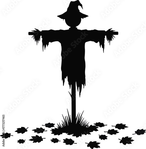 Silhouette of a spooky scarecrow standing in a field with fallen leaves in autumn