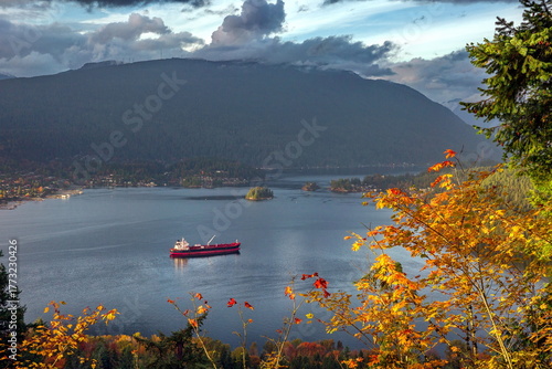 Vancouver Harbor, Ocean Ship in  Deep Cove on the background scenery of snow-capped mountains and stormy sky. Autumn time yellow trees on the slope in the foreground
