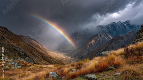 A stunning rainbow arcs over a mountain valley, illuminated against a stormy sky