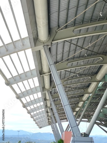 Modern airport or transit terminal canopy structure, underneath view of steel beams and industrial roofing.