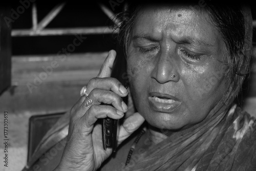 Photography Monochrome image of a senior Indian woman talking on the phone, black and white background reflects vulnerability and loneliness as AI scammer targets the elderly in bank fraud