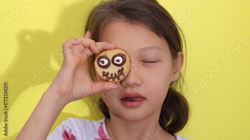 A child holding Halloween cookies shaped like spiders with chocolate and candy decorations near face