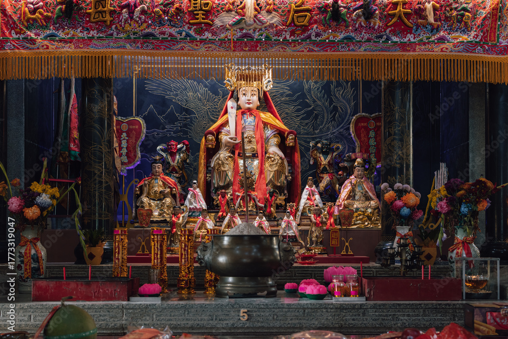 Fototapeta premium Golden statue of a deity sitting on a throne inside a chinese temple, surrounded by offerings and smaller statues