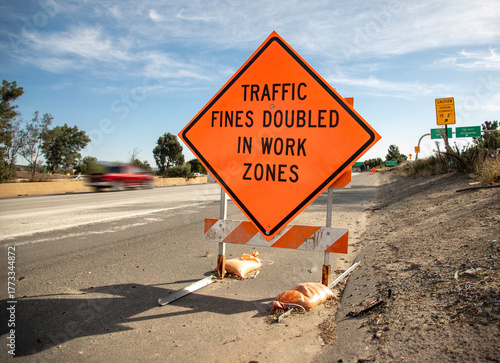 Orange traffic sign stating Traffic Fines Doubled in Work Zones with traffic in the background