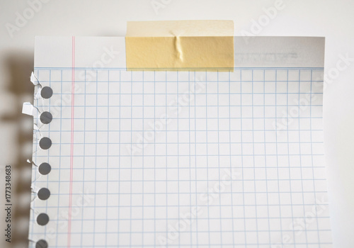 A sheet of graph paper with a hole punch and torn edges, held by tape