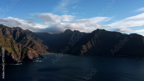Majestic Mountain Range Meets Deep Blue Ocean Under Cloudy Sky.