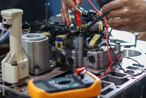 Hands of a technician using a multimeter to check the wiring and solenoid components of an automatic transmission valve body during diagnostic testing and repair.