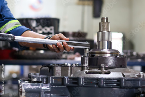 Mechanic's hands tightening a series of nuts on a heavy metal machine component using a torque wrench during precise assembly or industrial equipment repair.