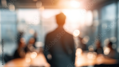 Wallpaper Mural A silhouetted figure stands in an office, illuminated by warm sunlight, with blurred colleagues in the background, creating a professional and contemplative atmosphere. Torontodigital.ca