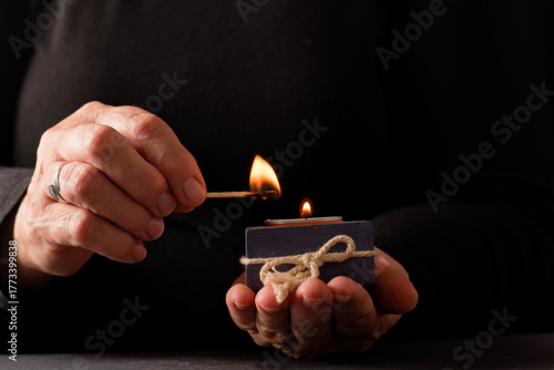 Quadro em tela hands of a woman lighting a candle with a match with a black background and copy
