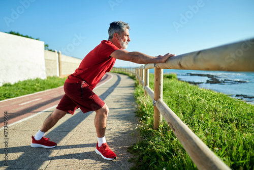 Senior man stretching legs after running on beach path