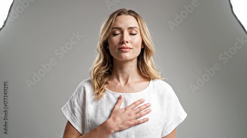 Woman with hand on chest, eyes closed in studio, neutral background