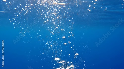 Underwater view of blue water with floating bubbles and sunlight.
