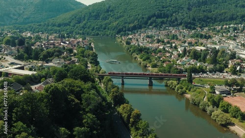 Wallpaper Mural Aerial view of a train moving across a bridge over the Neckar River in Germany, with a cruise ship navigating the river and a town nestled in the forested Odenwald valley. Torontodigital.ca