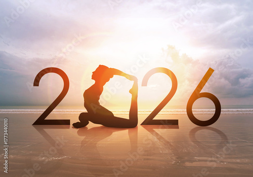 Happy new year card 2026. Silhouette of healthy girl doing Yoga One Legged Pigeon pose on tropical beach with sunset sky background, woman practicing yoga as a part of the Number 2026 sign.
