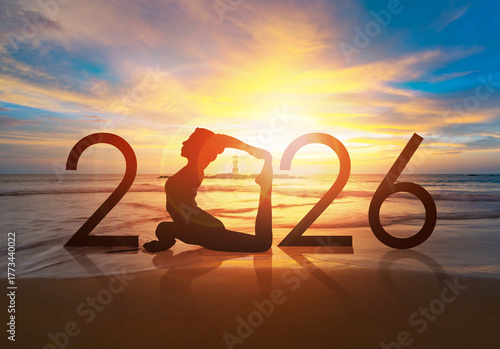 Happy new year card 2026. Silhouette of healthy girl doing Yoga One Legged Pigeon pose on tropical beach with sunset sky background, woman practicing yoga as a part of the Number 2026 sign.