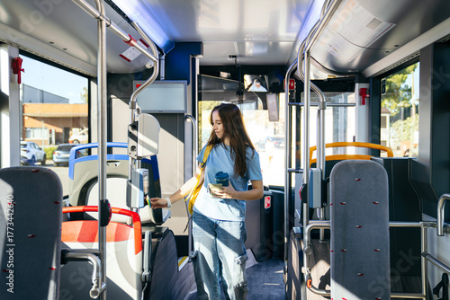 Obraz na plátně Young woman taps a contactless card to pay bus fare while commuting through a su