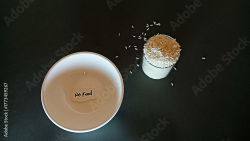Fotografie Conceptual image showing an empty bowl with a note “No Food” beside a glass filled with rice, symbolizing hunger, poverty, food crisis, inequality, and the importance of food security