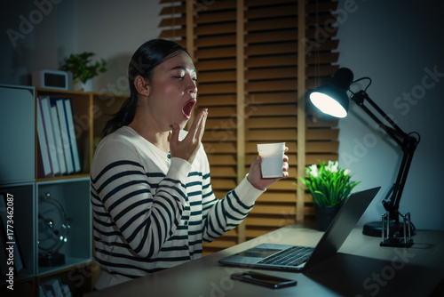 sleepy woman yawning while working with laptop at night
