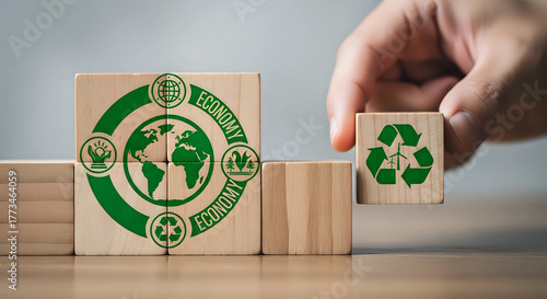 Hand placing wooden block with recycling symbol onto larger block with earth and recycling symbol