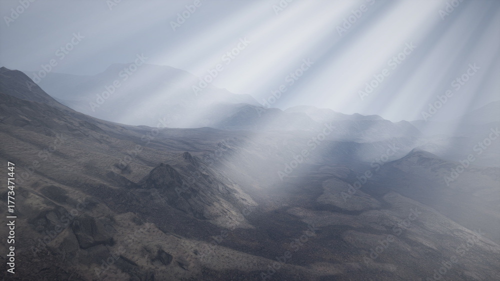 Obraz premium Radiant beams of light break through the clouds, illuminating a vast and rugged mountain terrain. The dramatic interplay of shadows and highlights creates an awe inspiring atmosphere at dawn.