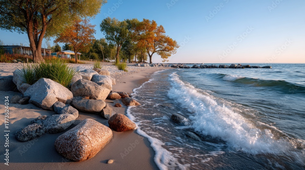 Obraz premium Serene Lakeshore With Gentle Waves Under Golden Sunlight And Autumn Trees In Warm Colors With Rocky Beach And Clear Blue Sky
