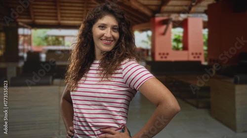 Wallpaper Mural Young hispanic woman with hands on hips posing in hotel lobby near reception desk wearing white and pink striped t shirt and jeans; confidence. Torontodigital.ca